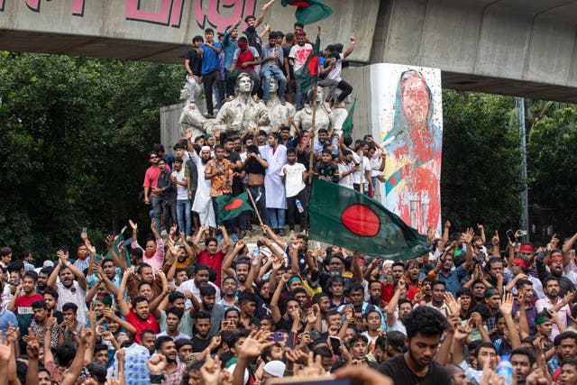 <p>Protesters climb a public monument as they celebrate after getting the news of Prime Minister Sheikh Hasina's resignation, in Dhaka</p>